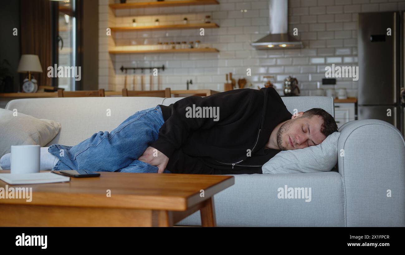 Müder Mann legt sich auf das Sofa und macht ein Nickerchen mit lässigen Klamotten. Erholung und Entspannung nach einem anstrengenden Arbeitstag und Pause im Wohnzimmer zu Hause. Stockfoto