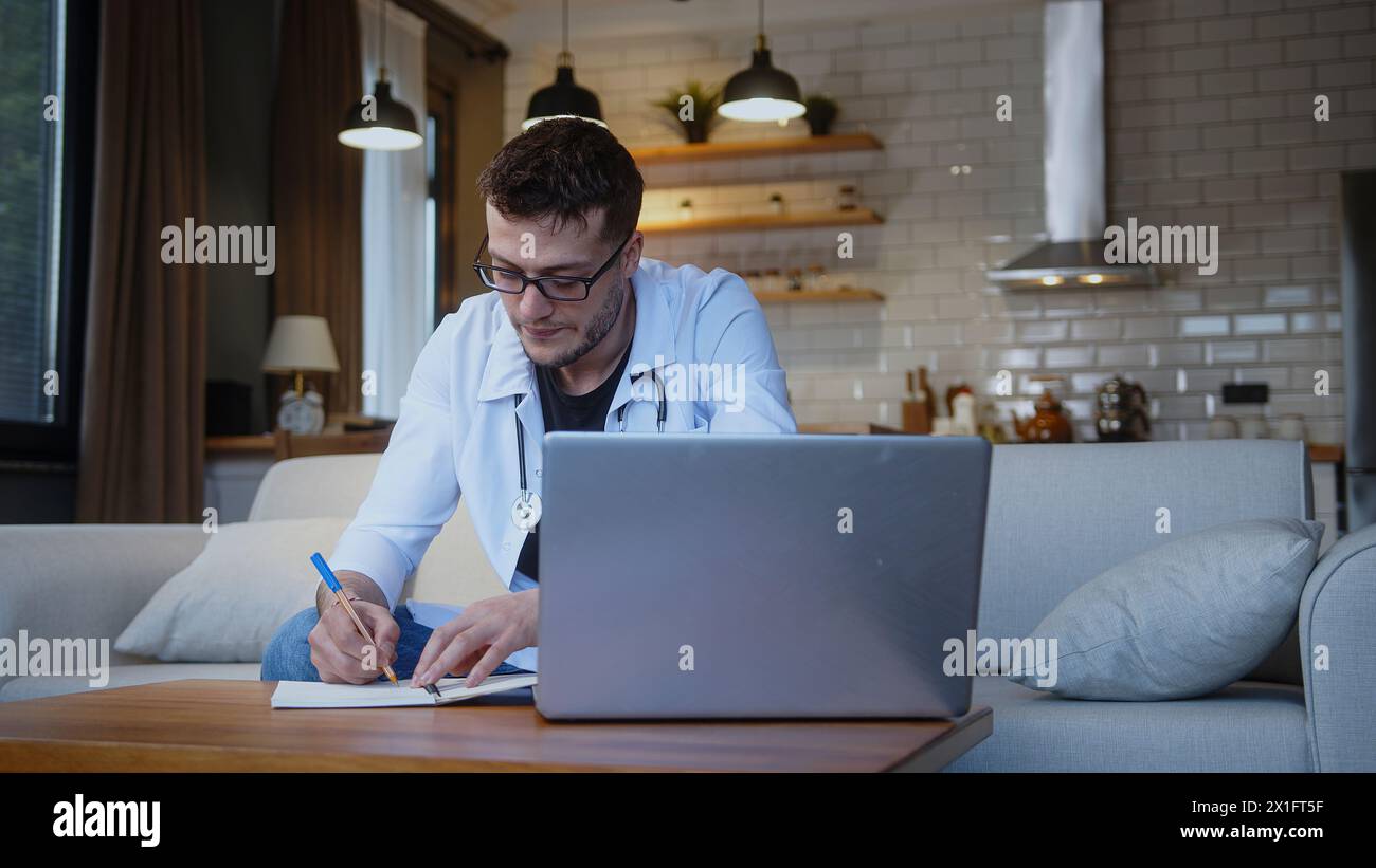 Professioneller junger männlicher Arzt mit Brille tragen weiße Uniform mit Stethoskop und haben Online-Konferenz-Videoanruf mit Patient durch in Laptop W Stockfoto