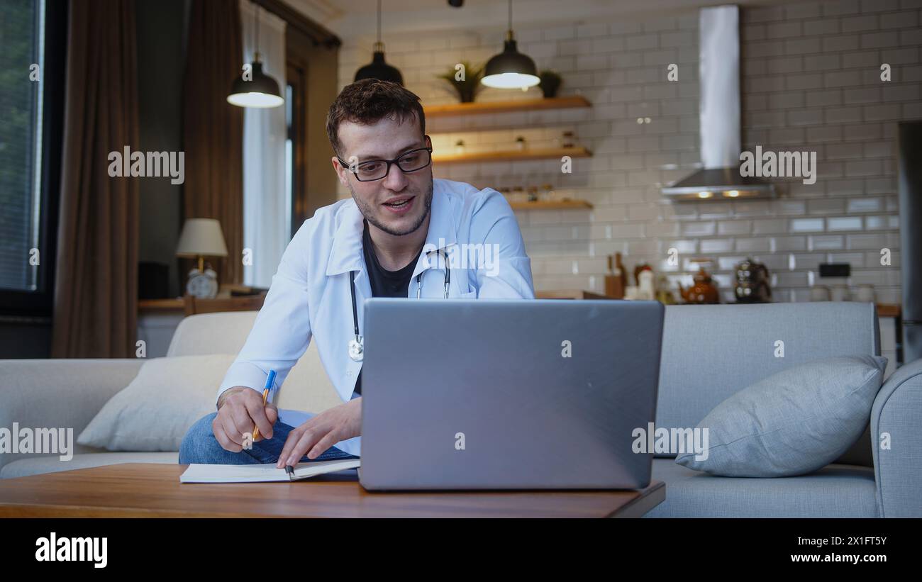 Professioneller junger Arzt mit Brille tragen weiße Uniform mit Stethoskop und haben Online-Konferenz-Videoanruf mit Patienten durch Laptop-Webcam Stockfoto