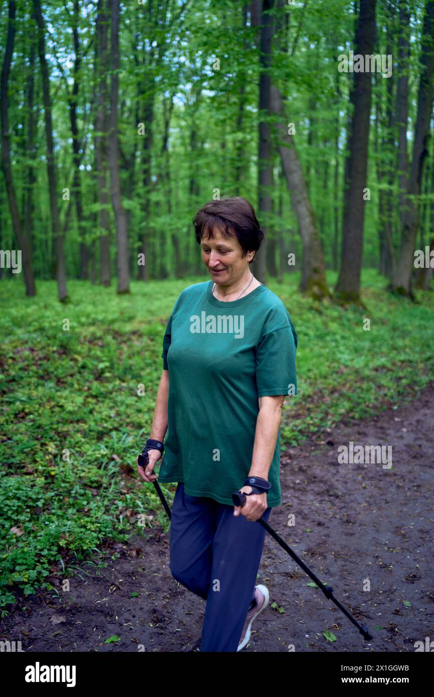 Eine ältere Frau macht Nordic Walking mit Stöcken im Frühlingswald Stockfoto