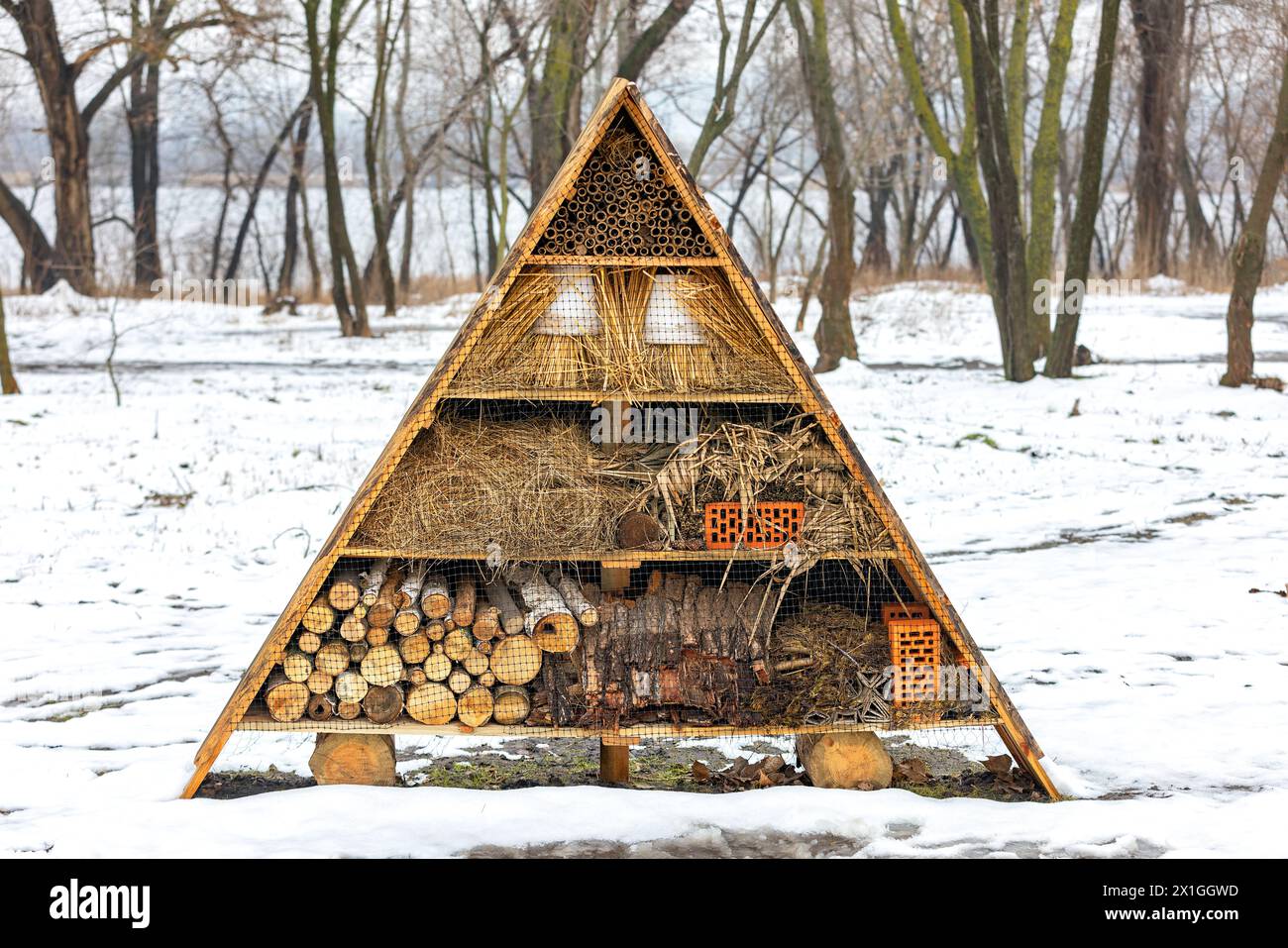 Ein Winterhotel für Insekten im Schnee aus Stroh, Bambusstöcken, Ziegeln, Fliesen, Flusskieseln, Baumrinde und röhrenförmige Stiele. Stockfoto