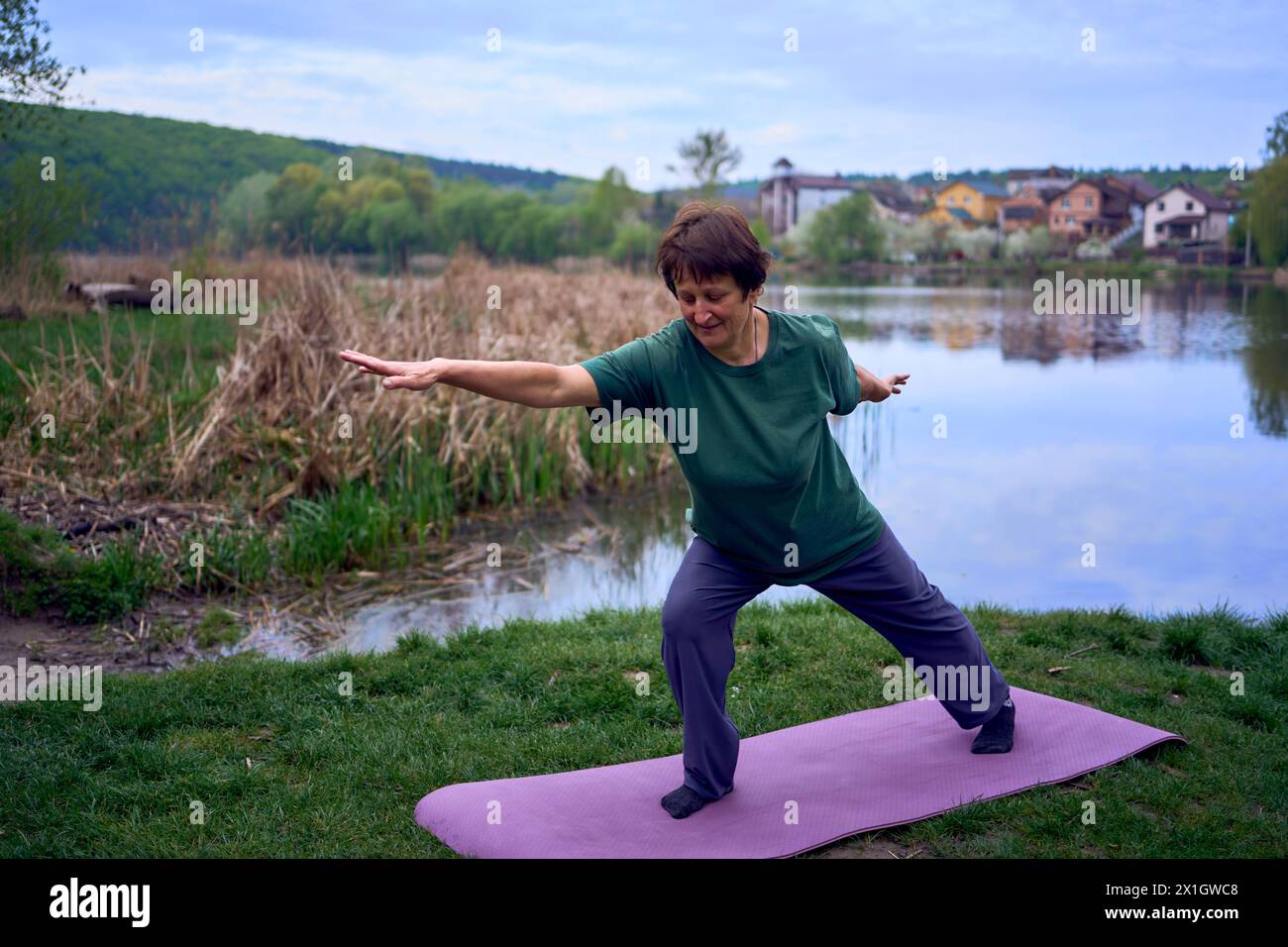 Eine alte Frau praktiziert morgens am Flussufer Yoga, kam von zu Hause mit dem Fahrrad Stockfoto