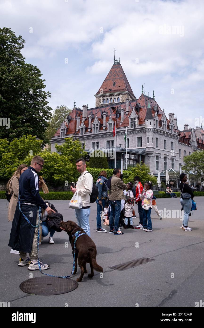 Eine Gruppe junger Menschen mit Hund vor dem Chateau d'Ouchy, einem luxuriösen neogotischen Hotel, das in einer Burg aus dem 12. Jahrhundert am Ufer des Gänsesees erbaut wurde Stockfoto