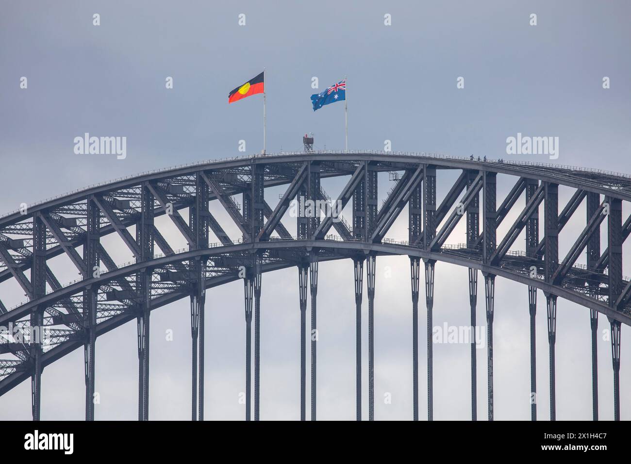 Die berühmte Sydney Harbour Bridge, die Flaggen der Aborigines und australiens, die auf dem Gipfel fliegen, die Menschen, die den Bogen vom Brückenkletterausflug hinunterlaufen, Sydney, NSW Stockfoto