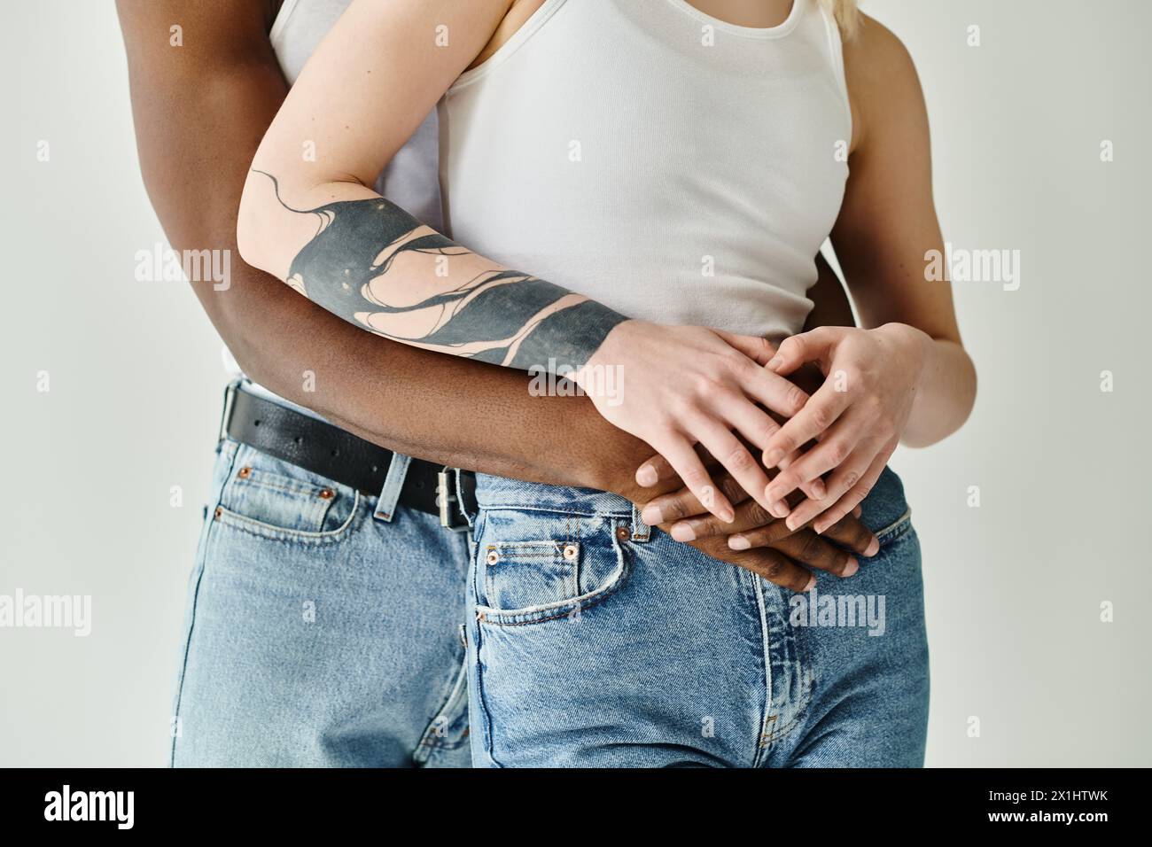 Ein Mann mit einem Tattoo am Arm, der eine Frauenhand hält, zeigt Einheit, Liebe und Verbindung zwischen einem multikulturellen Paar in einem Studio auf grauem Rücken Stockfoto