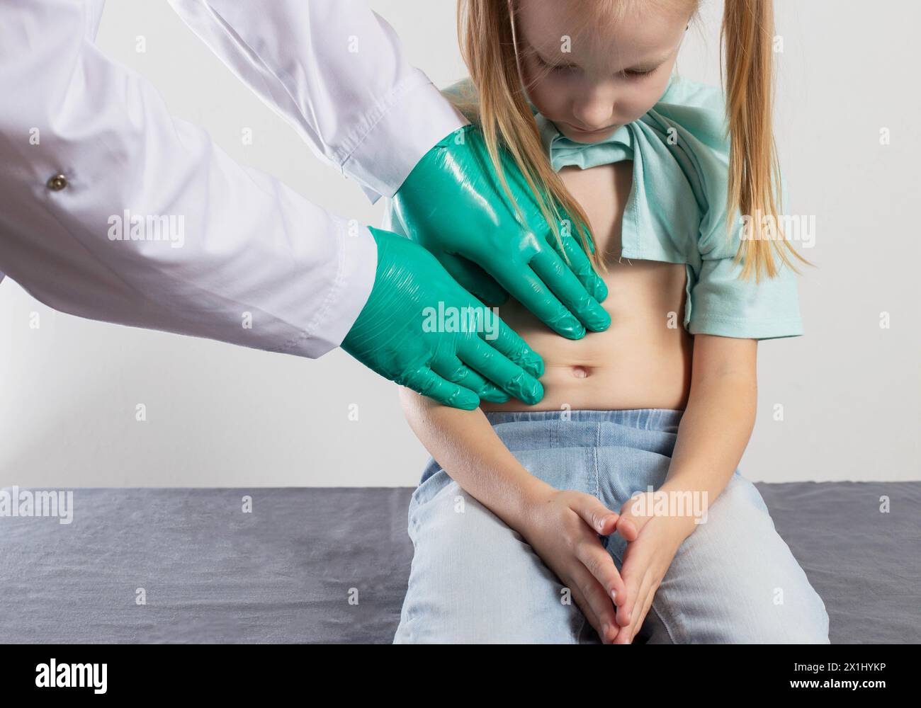 Die Hände eines Therapeuten-Arztes palpieren den Bauch eines kleinen siebenjährigen Mädchens auf Organkater. Entzündung der Bauchorgane, Dyspepsi Stockfoto
