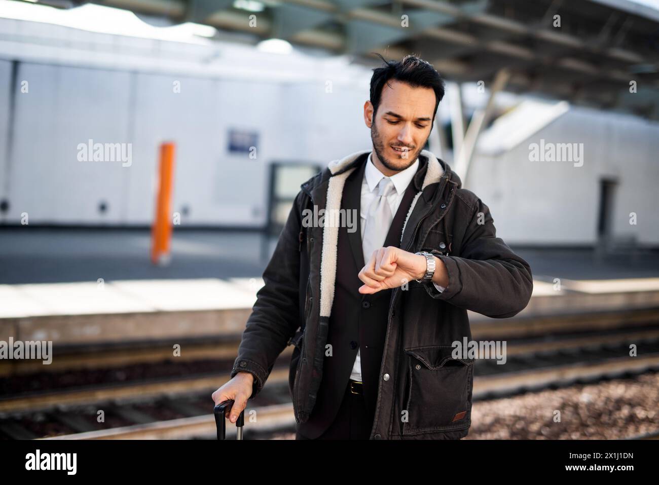 Ein junger Berufsmann blickt auf seine Uhr, während er an einem sonnigen Tag auf den Zug wartet Stockfoto