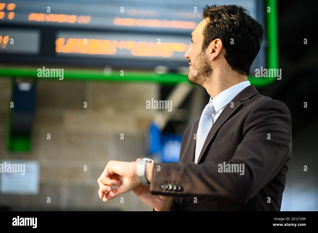 Ein gut gekleideter Mann blickt auf seine Uhr, während er in einem modernen Bahnhof auf seinen Zug wartet Stockfoto