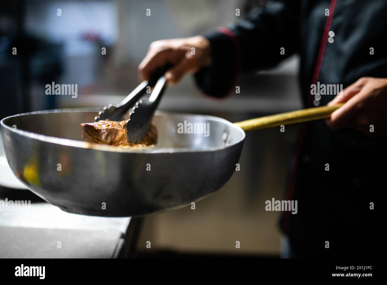 Nahaufnahme eines Küchenchefs in einer Geschäftsküche, der ein Steak in einer Edelstahlpfanne perfekt anbraten lässt Stockfoto