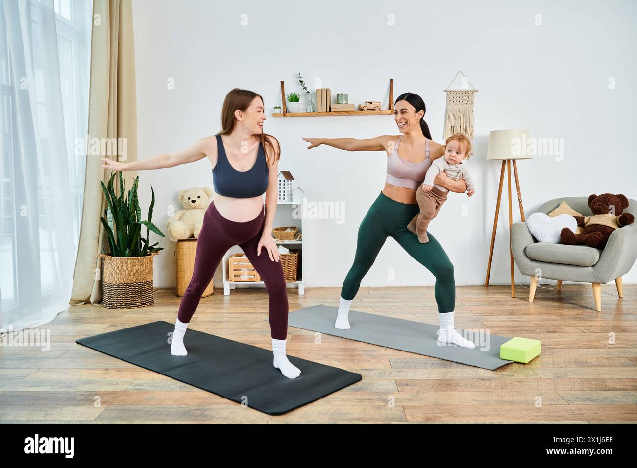 Eine junge, schöne Mutter und ihr Baby üben Yoga in einem gemütlichen Wohnzimmer unter Anleitung ihres Lehrers während der Elternkurse. Stockfoto