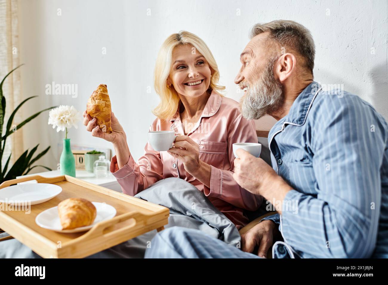 Ein reifes, liebevolles Paar in legeren Haushaltswaren, das gemeinsam an einem Tisch im Schlafzimmer eine Mahlzeit genießt. Stockfoto