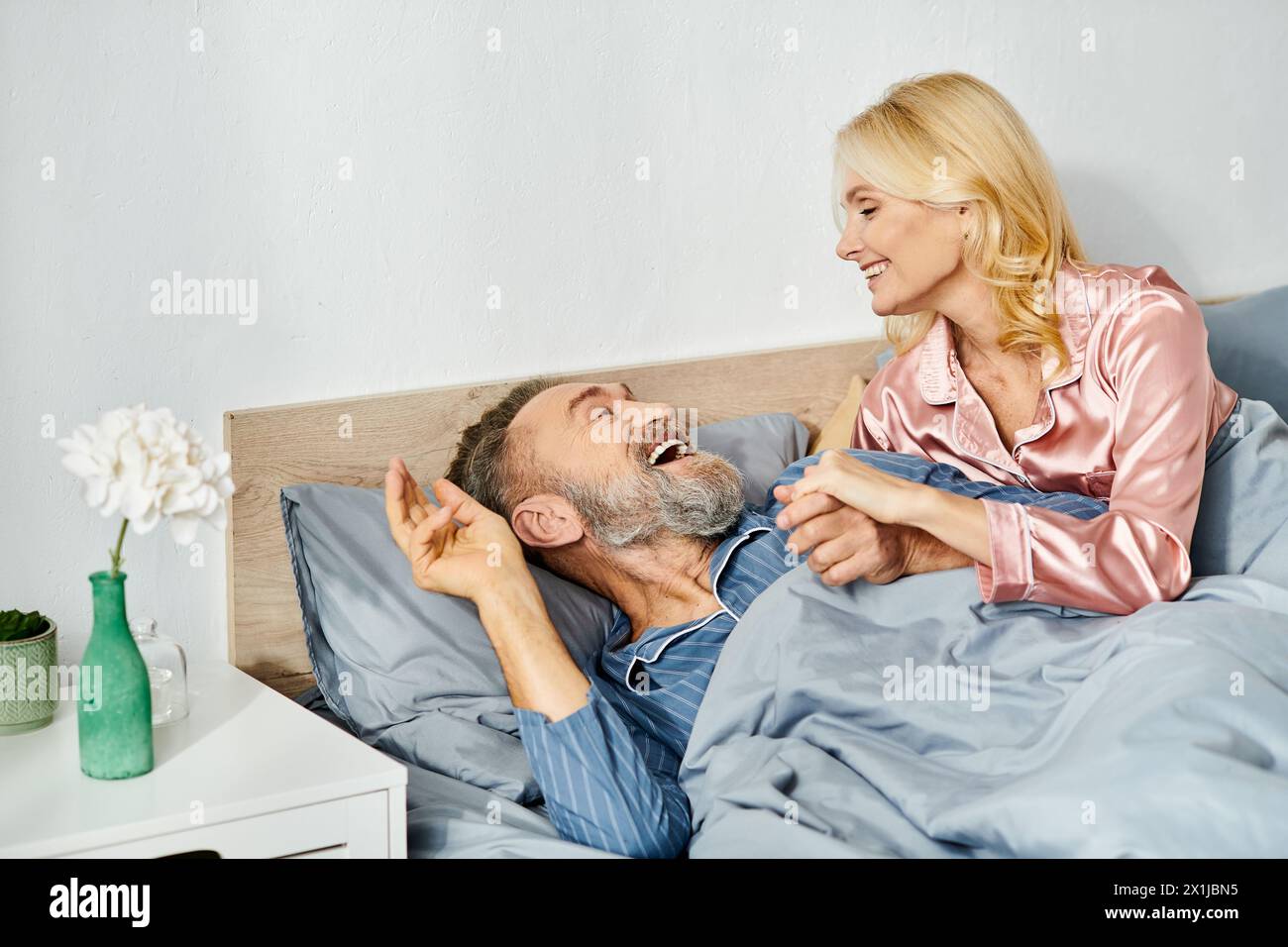 Ein Mann und eine Frau, ein reifes, liebevolles Paar, in gemütlicher Hauswäsche, liegen friedlich zusammen im Bett und teilen einen Moment der Intimität und Nähe. Stockfoto