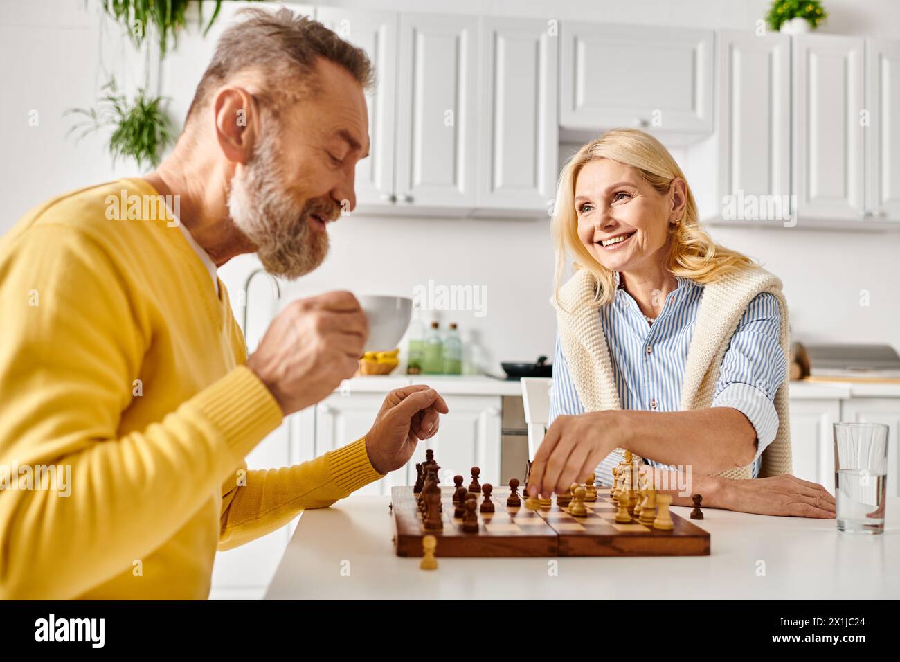 Ein reifer Mann und eine Frau in gemütlicher Heimkleidung spielen in einem Schachspiel, tief in Gedanken, während sie ihre nächsten Schritte planen. Stockfoto