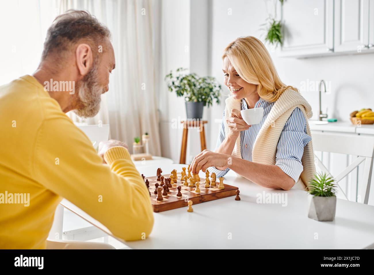 Ein reifes, liebevolles Paar in kuscheliger Homewear, das sich in einem intensiven Schachspiel engagiert, Strategien entwickelt und berechnete Bewegungen macht. Stockfoto
