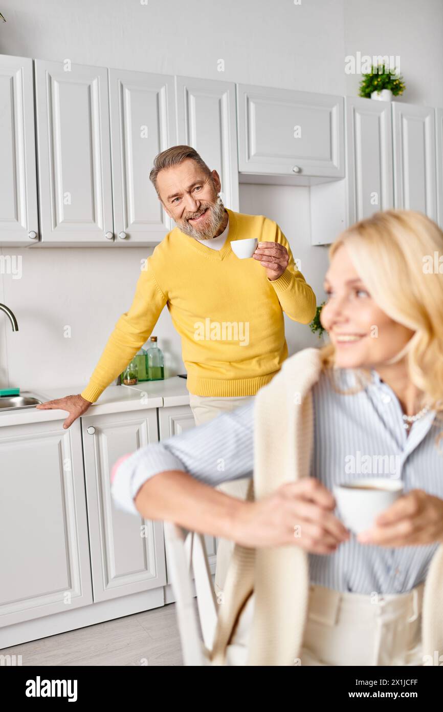 Ein reifes, liebevolles Paar in gemütlichen Haushaltswaren, das zusammen in einer Küche zu Hause steht und einen besonderen Moment teilt. Stockfoto