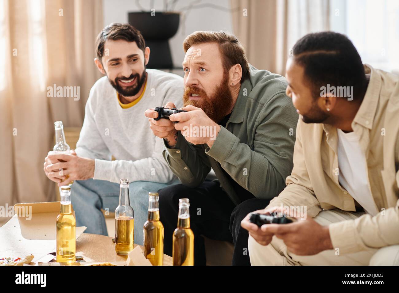 Drei fröhliche, interrassische Männer in lässiger Kleidung sitzen um einen Tisch, verbinden sich und genießen einander Gesellschaft, während sie Fernbedienungen halten. Stockfoto