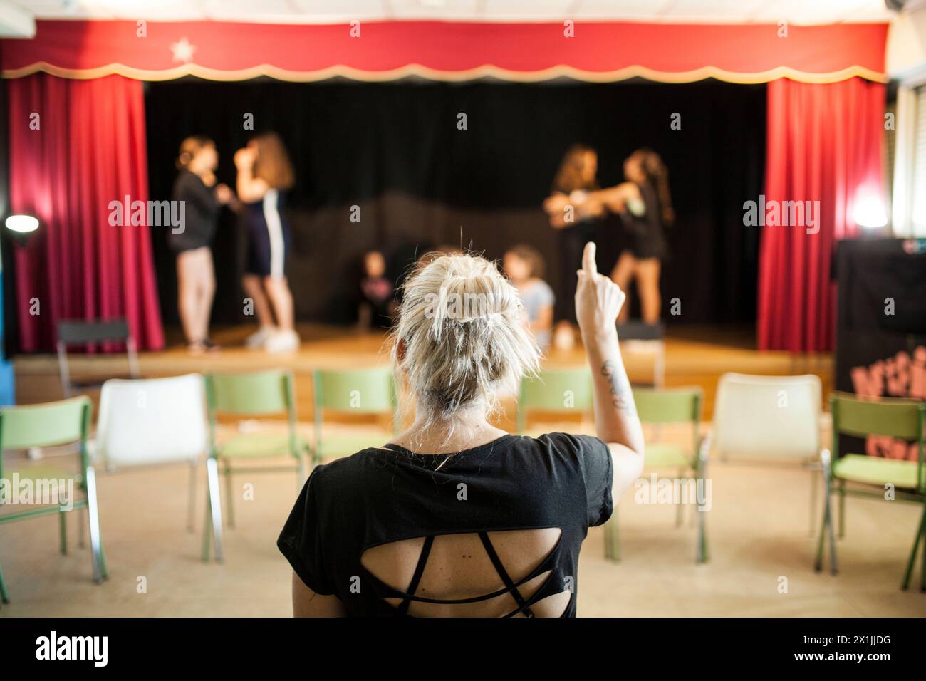 Mädchen loben einen Theaterunterricht vor dem Blick ihrer blonden Lehrerin auf dem Rücken Stockfoto