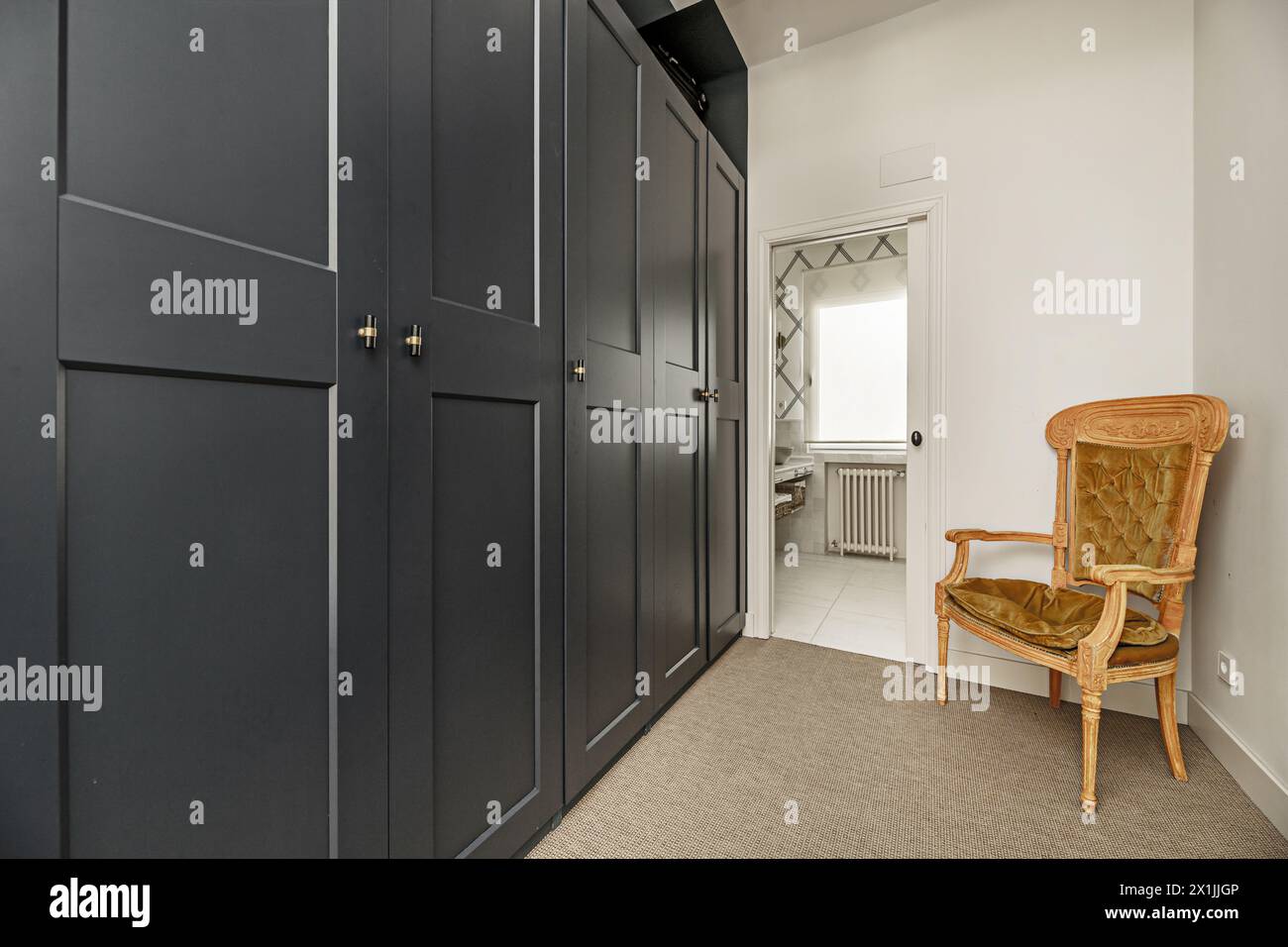 Der Flur führt zu einem Badezimmer mit benzingrün lackierten Holzschränken und einem Sessel im Louis XV-Stil mit klapprigen Kissen Stockfoto