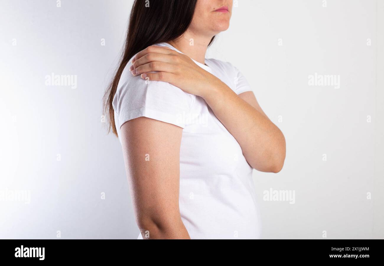 Ein Mädchen auf weißem Hintergrund hält ihre Schulter und hat Schmerzen. Das Konzept der Bursitis und des Schultergelenkschmerzes. Neuritis brachialis an Stockfoto