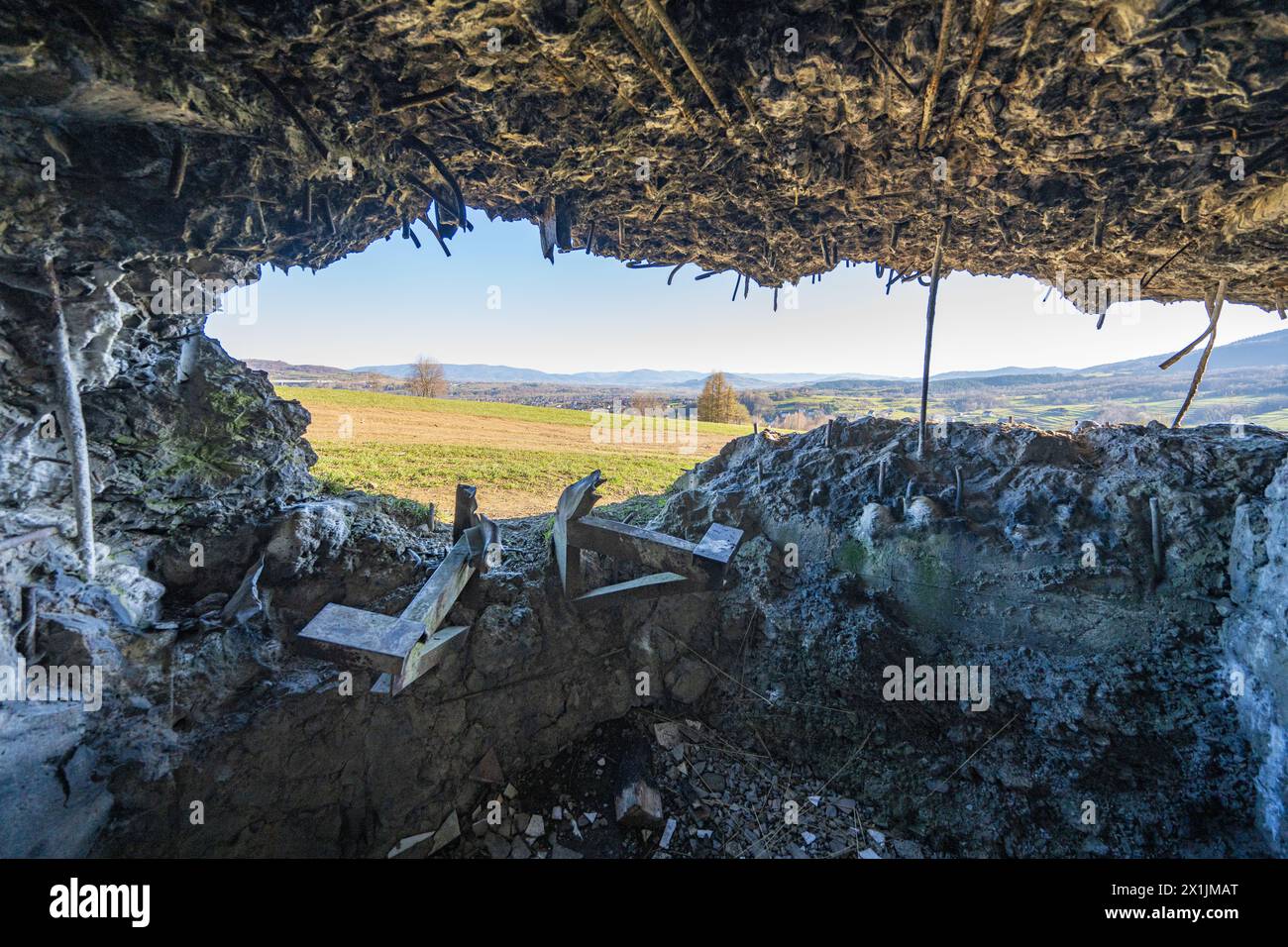Blick vom zerstörten Bunkerfenster auf die Wiese und die Hügel. Hervorstehende rostige Verstärkungsdrähte. Polen, Wyrwidab-Bunker, Wegierska Gorka. Stockfoto