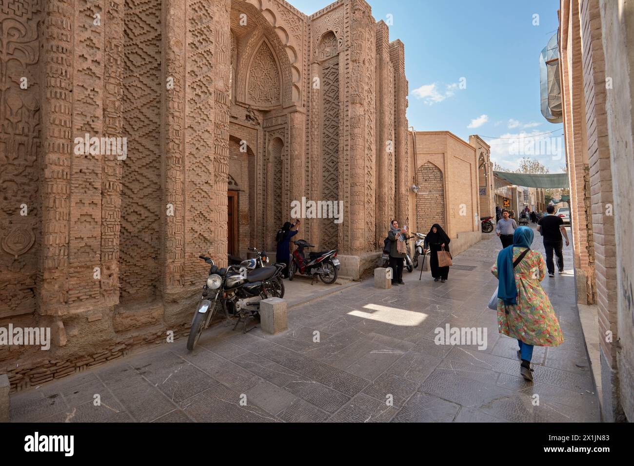 Die Menschen laufen in einer engen Straße am Jorjir-Tor, dem einzigen verbliebenen Teil der Jorjir-Moschee aus dem 10. Jahrhundert in Isfahan, Iran. Stockfoto