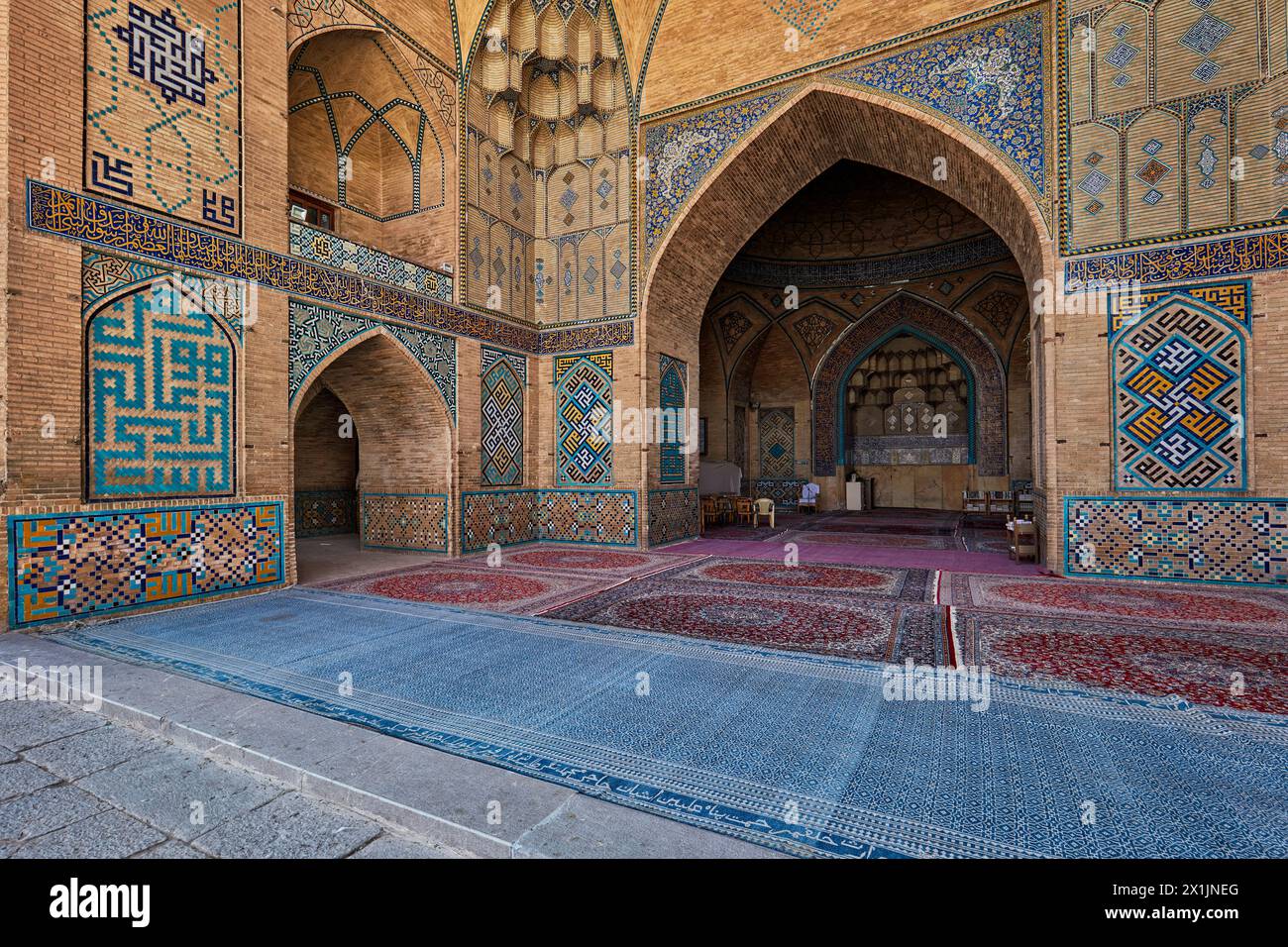 Blick von innen auf die Hakim-Moschee mit kunstvollen Fliesenmosaiken an den Ziegelwänden und Teppichboden. Isfahan, Iran. Stockfoto