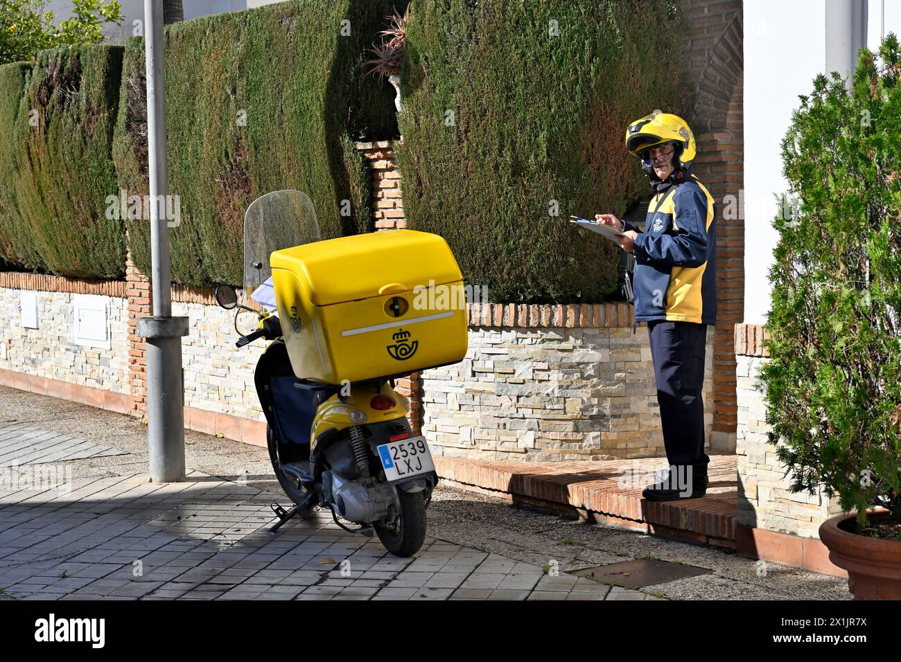 Spanischer Postbote, der kleine Pakete auf dem Motorrad vor der Tür des Kunden zustellt, Spanien Stockfoto