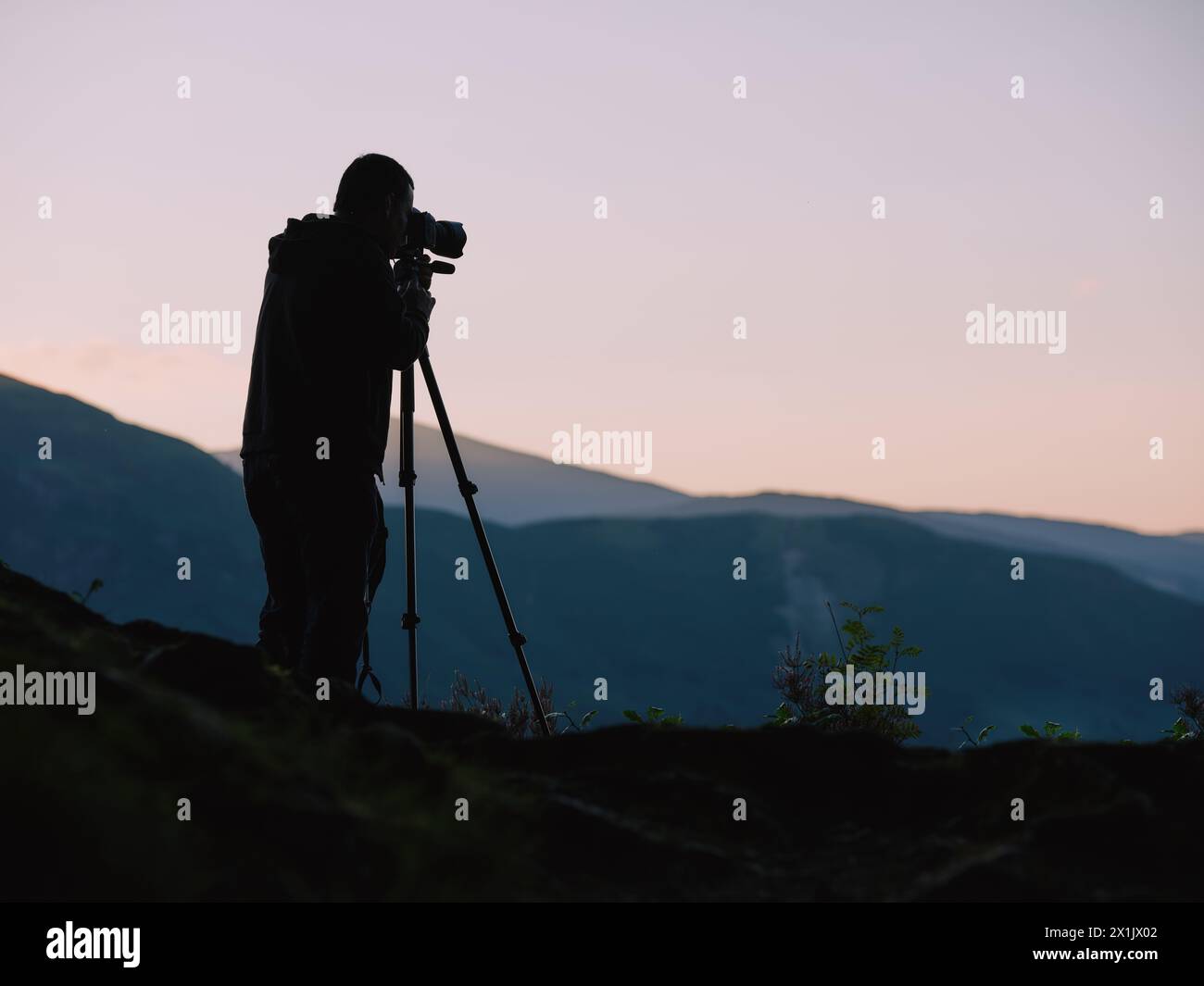 Eine Silhouette eines Landschaftsfotografen mit Stativ und Kamera bei Sonnenuntergang in einer minimalen Berglandschaft. Stockfoto