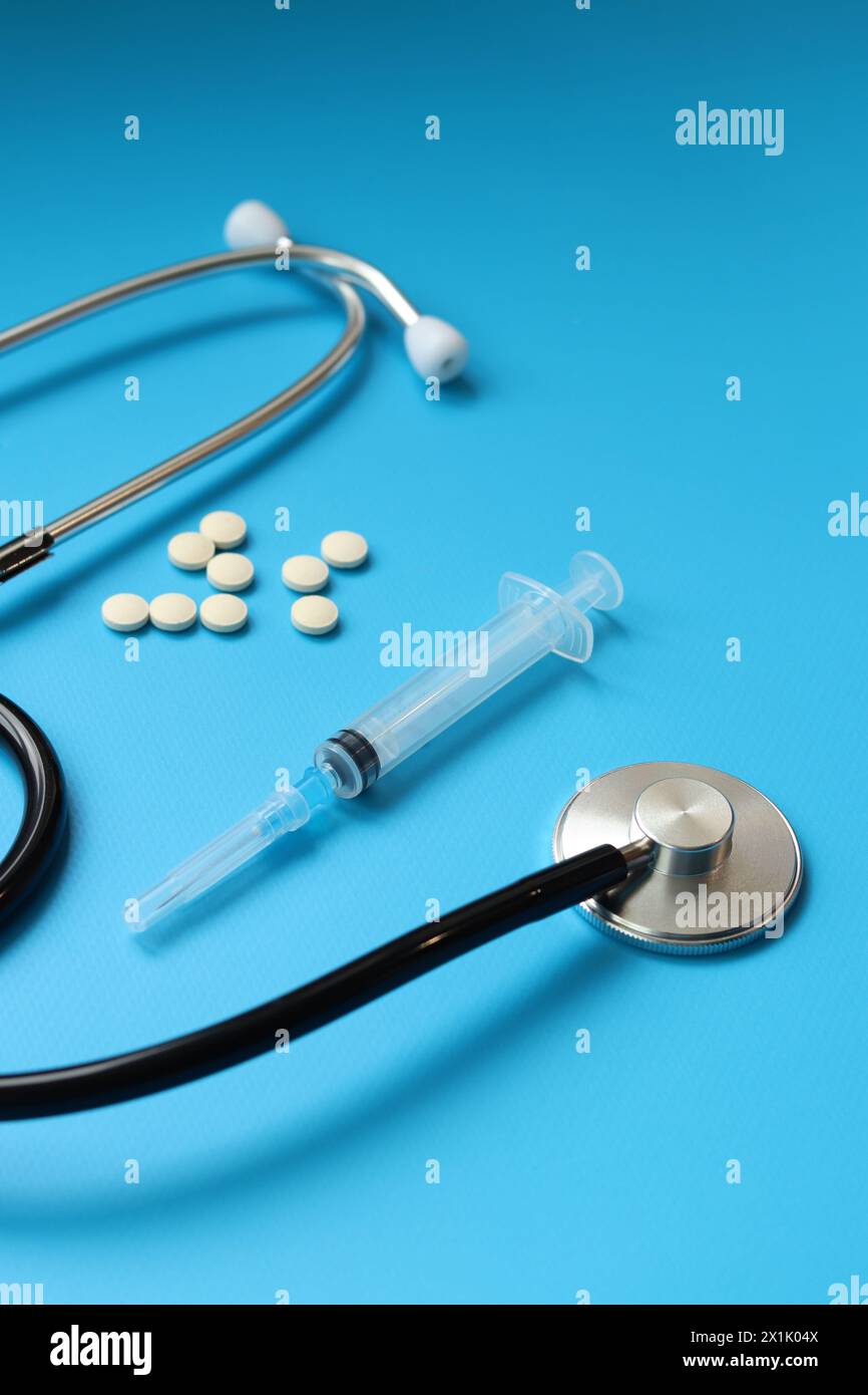 Stethoskop, Pillen und Spritze auf blauem Hintergrund, selektiver Fokus. Kardiologie und Gesundheitskonzept. Auskultationsgerät. Medizinisches Versorgungskonzept. Medi Stockfoto