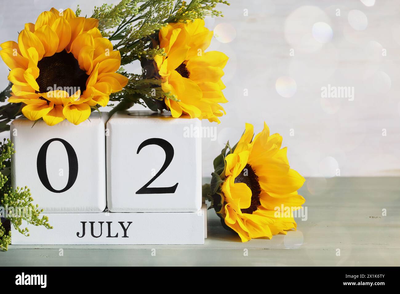 Besondere Erholung für den Behindertentag. Weiße Holzkalenderblöcke mit Datum 2. Juli und wunderschönem Sonnenblumenstrauß mit Bokeh. Selektiver Fokus Stockfoto
