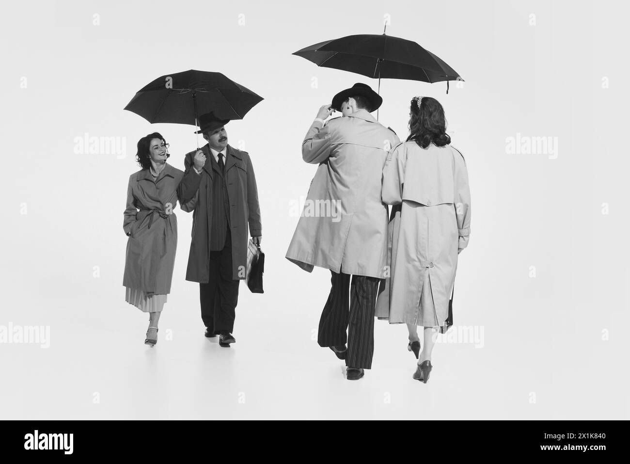 Zwei Paar in eleganten Cloches, Trenchcoat, die unter einem Regenschirm laufen. Schwarzweißbild. Begrüßung für ein Paar Stockfoto