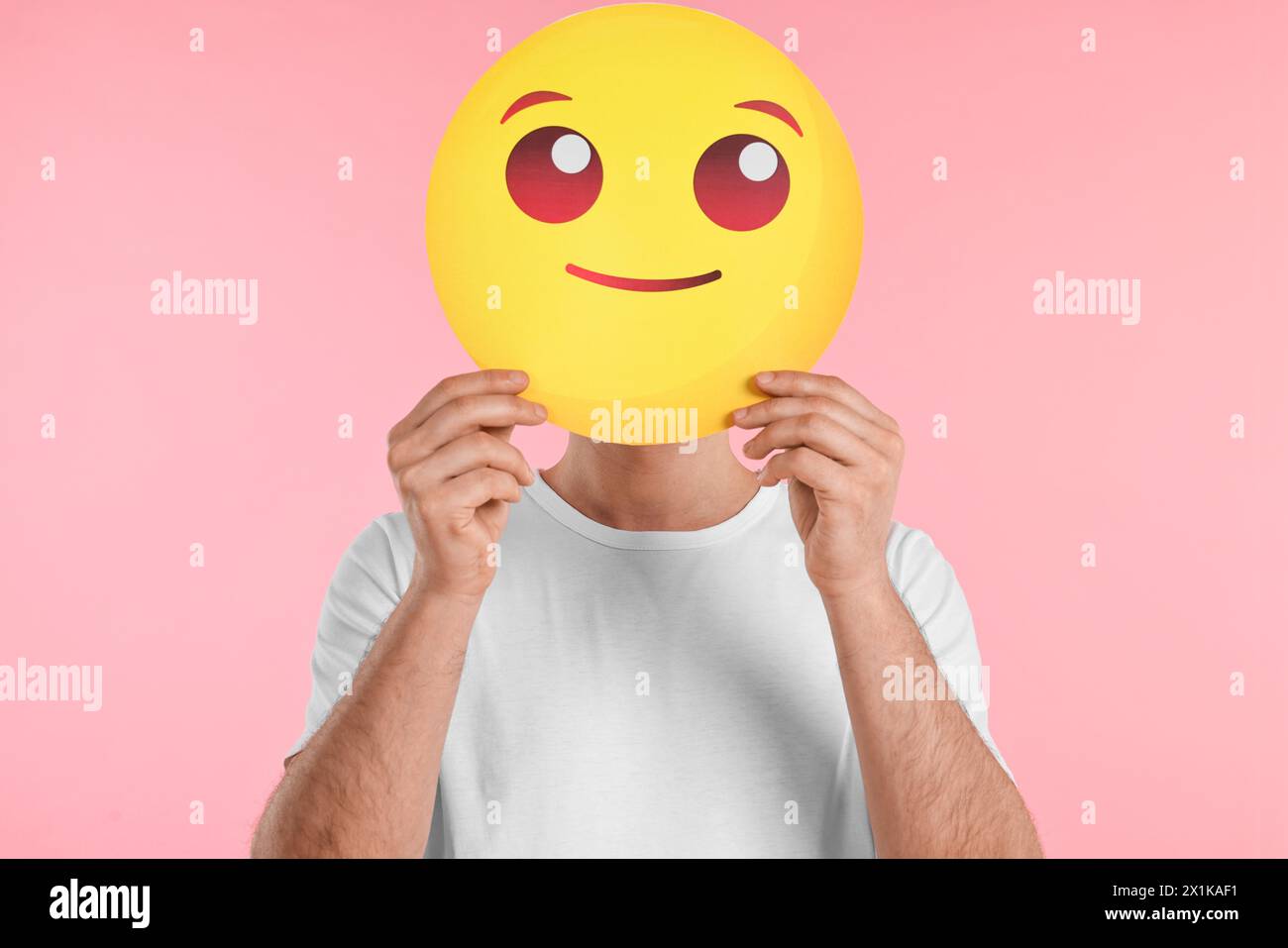 Mann bedeckt Gesicht mit lächelndem Emoticon auf rosa Hintergrund Stockfoto