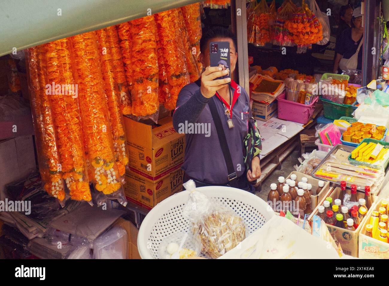 Maeklong, Thailand - Ein Stallhalter benutzt sein Smartphone, um den Zug zu erfassen, der ganz in der Nähe der Stände durch den Bahnmarkt fährt Stockfoto