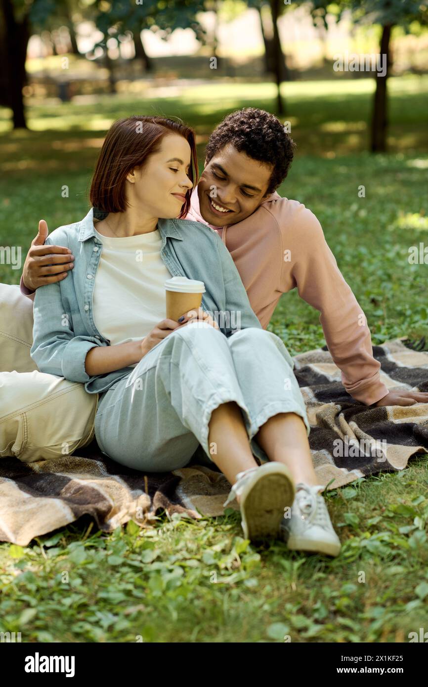 Ein Mann und eine Frau in lebendiger Kleidung sitzen auf einer Decke im Park und genießen sich in Gesellschaft der anderen in der Schönheit der Natur. Stockfoto