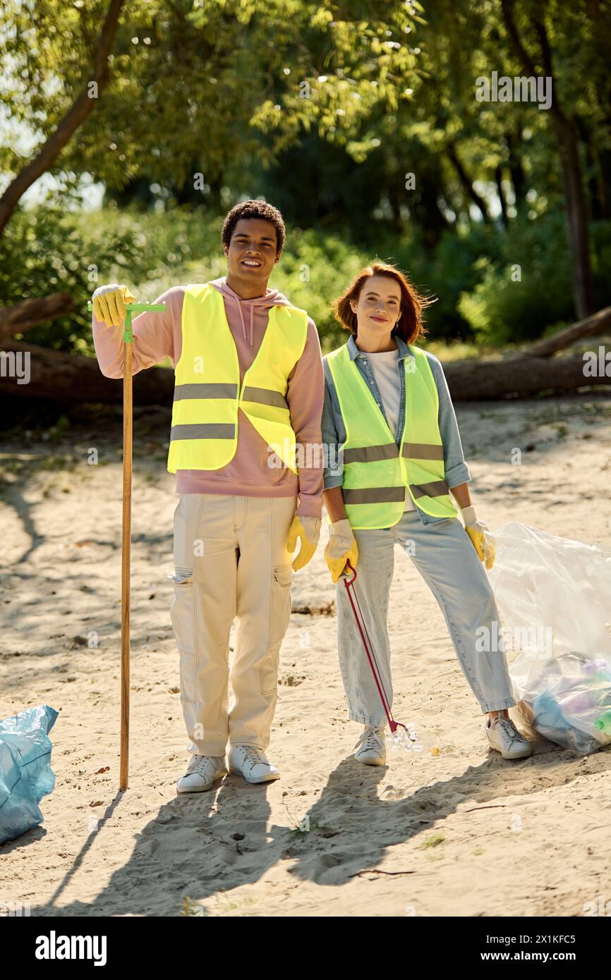 Ein sozial aktives, vielfältiges Paar mit Sicherheitswesten und Handschuhen steht am Strand vereint. Stockfoto