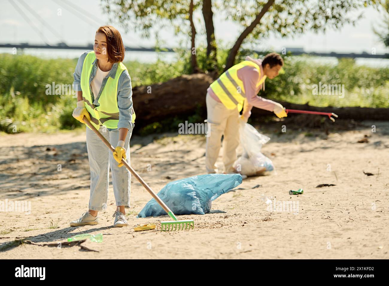 Ein liebevolles Paar, das Sicherheitswesten und Handschuhe trägt, im Sand steht und gemeinsam einen Park reinigt, um die Umwelt zu schonen. Stockfoto