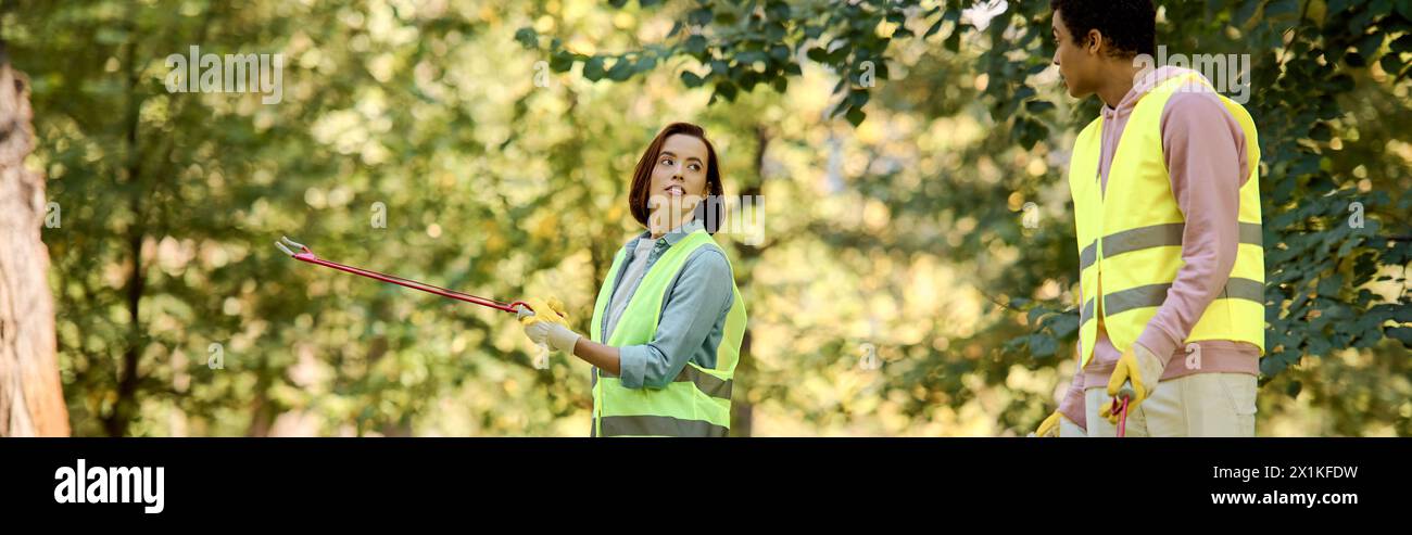 Ein vielseitiges, liebevolles Paar, in Sicherheitswesten und Handschuhen gekleidet, steht im ruhigen Wald. Stockfoto
