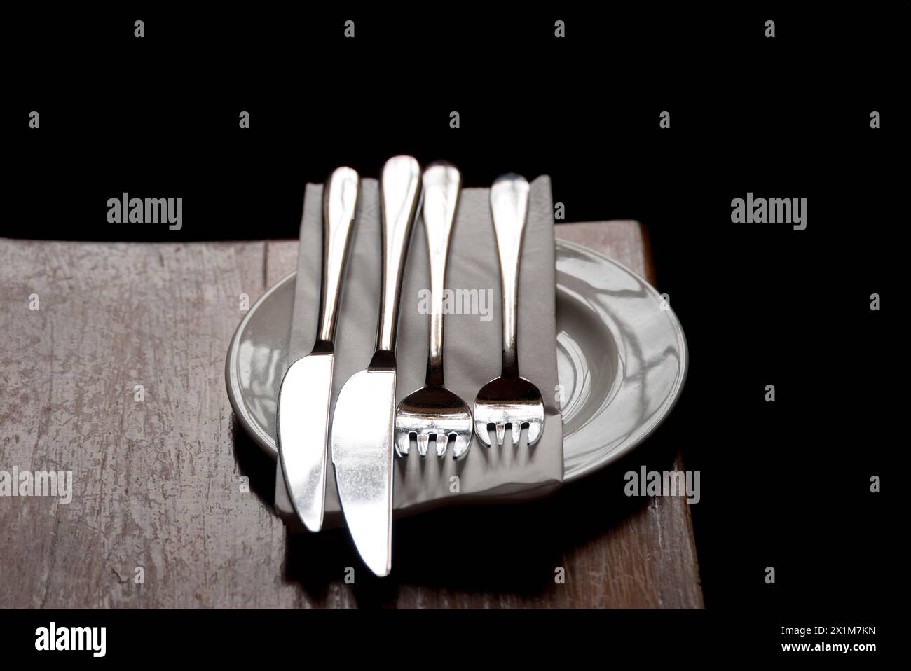 Stellen Sie Messer, Gabeln und Serviette auf einen weißen Teller auf einen rustikalen Holztisch Stockfoto