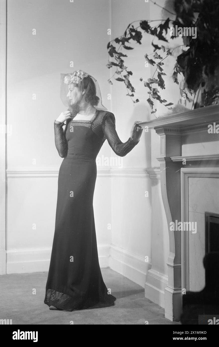 LONDON FASHION DESIGNERS: DIE ARBEIT VON MITGLIEDERN DER INCORPORATED SOCIETY OF LONDON FASHION DESIGNERS, LONDON, ENGLAND, UK, 1945 - Ein Model trägt einen schwarzen Dinner-Gehrock des Modedesigners Peter Russell. Das Kleid hat ein Fischnetz am Rücken, an den Armen und am Saum. Stockfoto