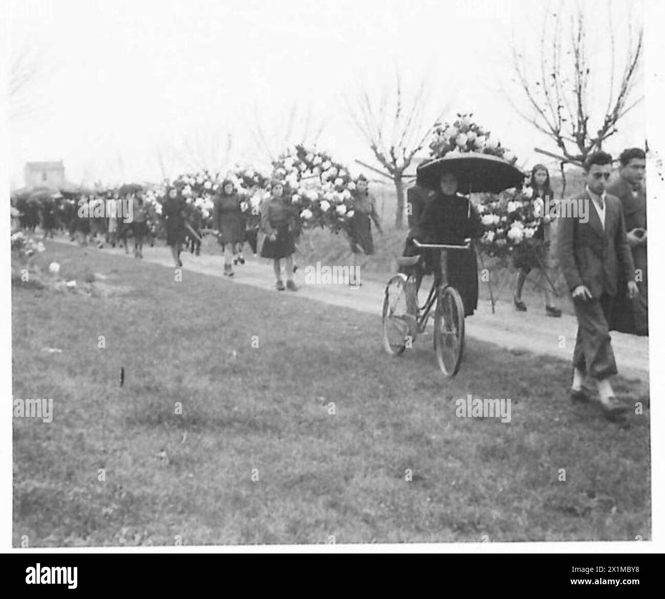 Italienische Frauen tragen Kränze hinter dem Sarg eines Partisanen während einer Beerdigung, die von britischen Armeeangehörigen beobachtet wird. Stockfoto