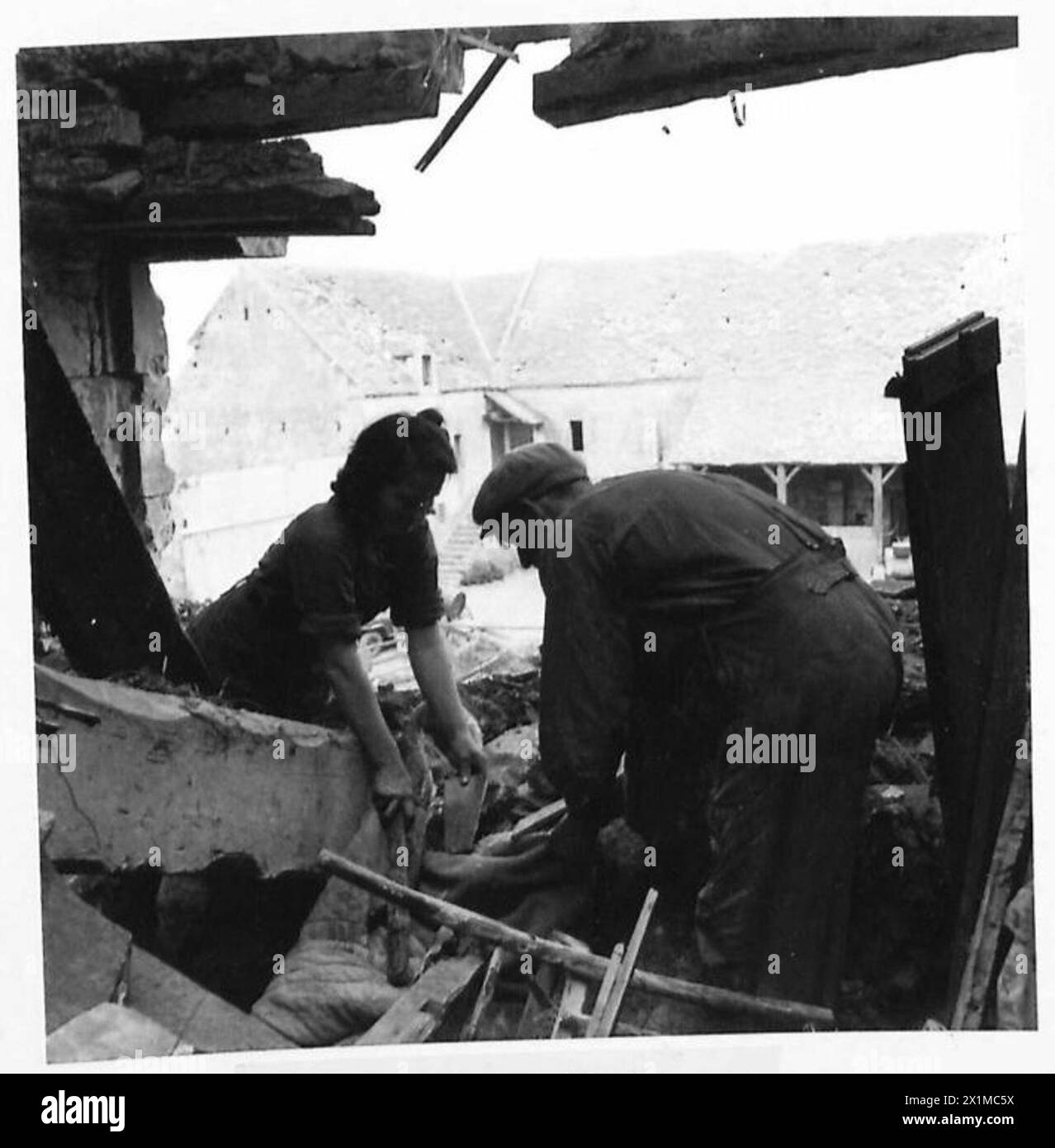 Die Landarbeiter Marie und Pierre holen Decken aus Trümmern in einem französischen Bauernhaus, das durch Schussfeuer beschädigt wurde, und andere beschädigte Bauernhäuser sind sichtbar, britische Armee, 21. Armeegruppe. Stockfoto