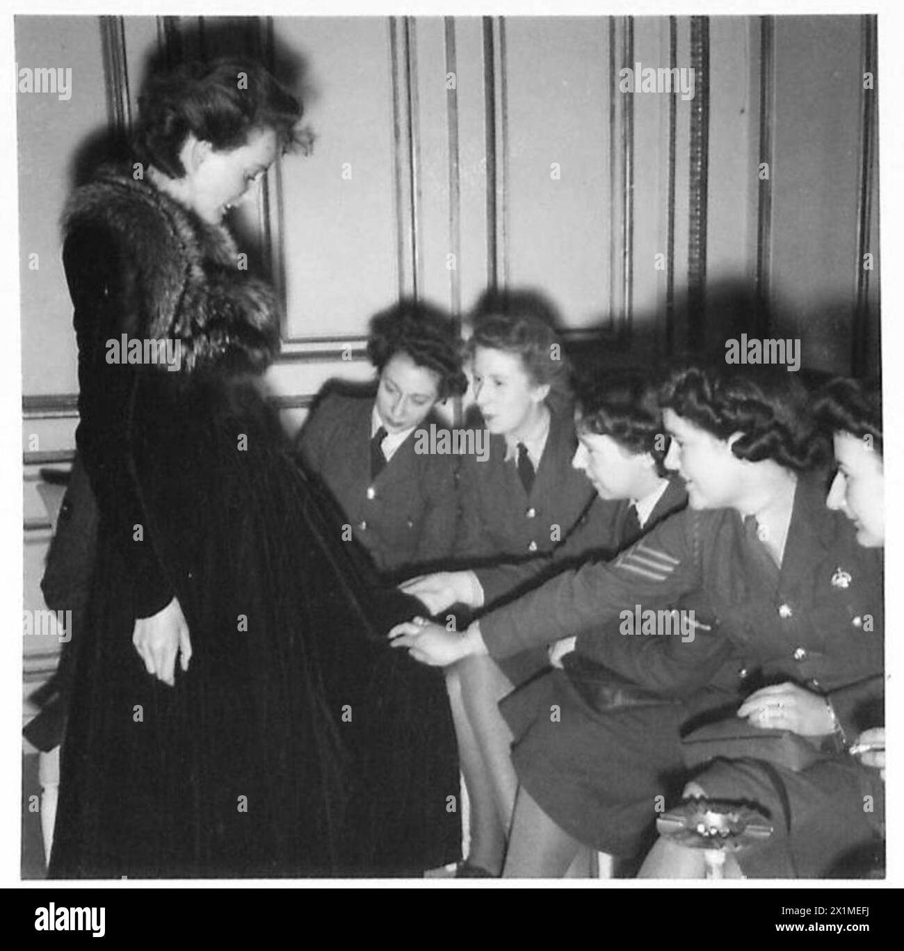 Britische Militärfrauen, die auf einer Pariser Modenschau teilnehmen, untersuchen die Qualität und Verarbeitung eines ausgestellten Modells, der 21. Armee-Gruppe. Stockfoto