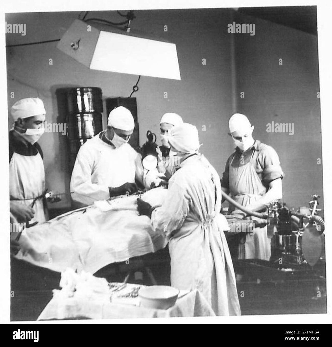 Raymond breit hilft einem britischen Chirurgen, indem er eine Lampe im Operationssaal einer Notfalloperationsstation hält, während der American Field Service-Operationen mit der britischen Eighth Army. Stockfoto