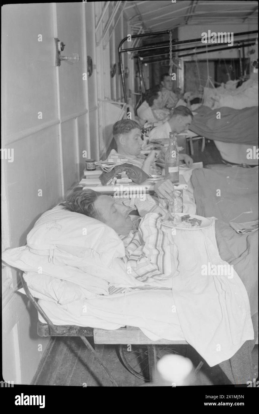 REHABILITATION BRITISCHER SOLDATEN AUS DER NORMANDIE: DIE ARBEIT DES ROBERT JONES AND DAME AGNES JAGDKRANKENHAUSES, OSWESTRY, SHROPSHIRE, ENGLAND, VEREINIGTES KÖNIGREICH, 1944 - Mahlzeiten auf der Station im Robert Jones and Dame Agnes Hunt Orthopaedic Hospital, Oswestry. Trooper L Holmes (im Vordergrund) muss seinen Teller auf seiner Brust ablegen, da er seinen Körper oder seine Beine nicht bewegen kann. Trooper Holmes stammt aus Bermondsey und diente beim Royal Armoured Corps, bevor er verwundet wurde Stockfoto