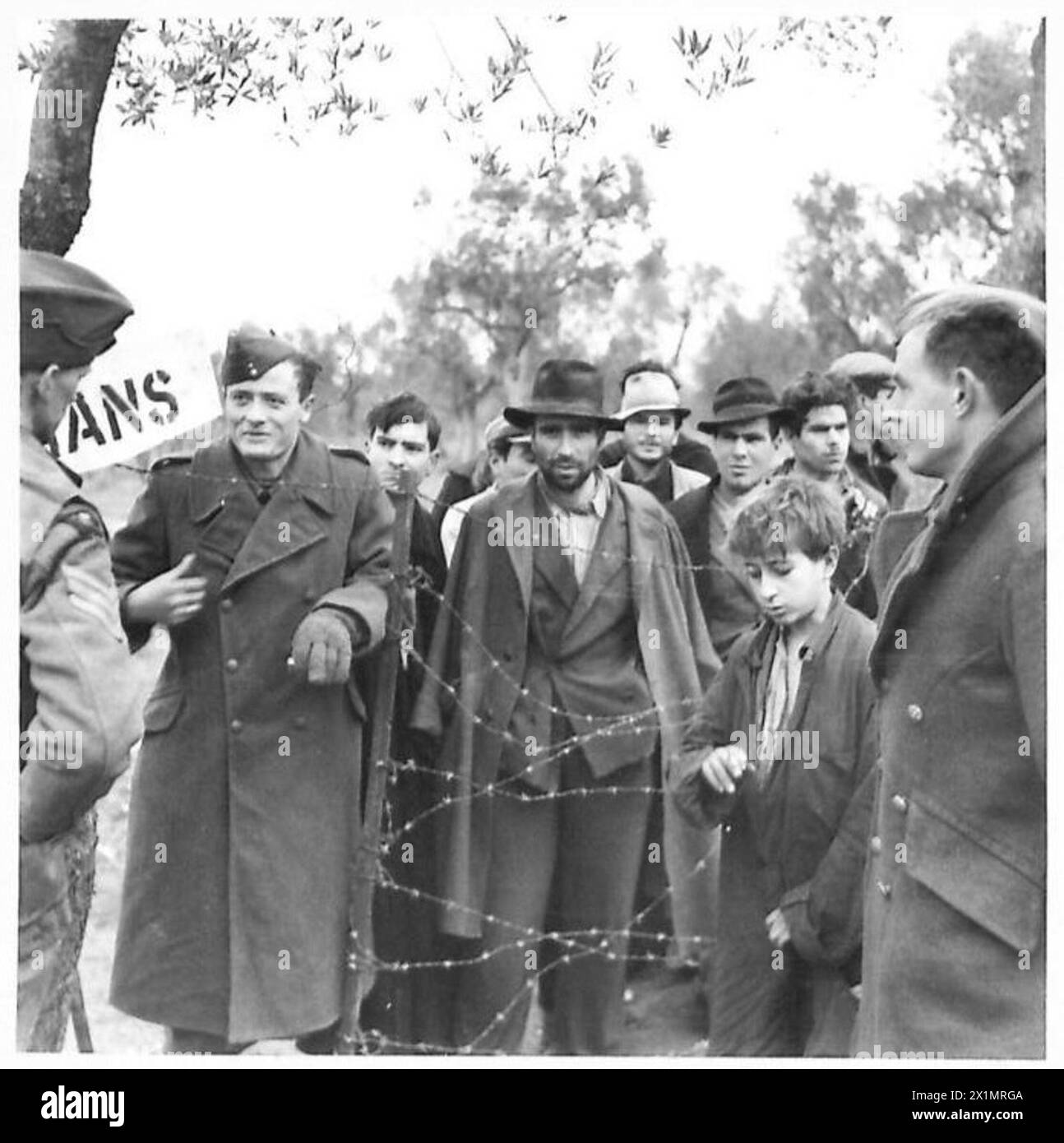 Italienische Zivilisten werden im Hauptquartier der Fünften Armeedivision unter bewaffneter Wache gefangen gehalten, während sie auf Verhöre warten; ein britischer Soldat meldete sich freiwillig als Kellner, blieb aber außerhalb des Schlachtfeldes der britischen Armee. Stockfoto