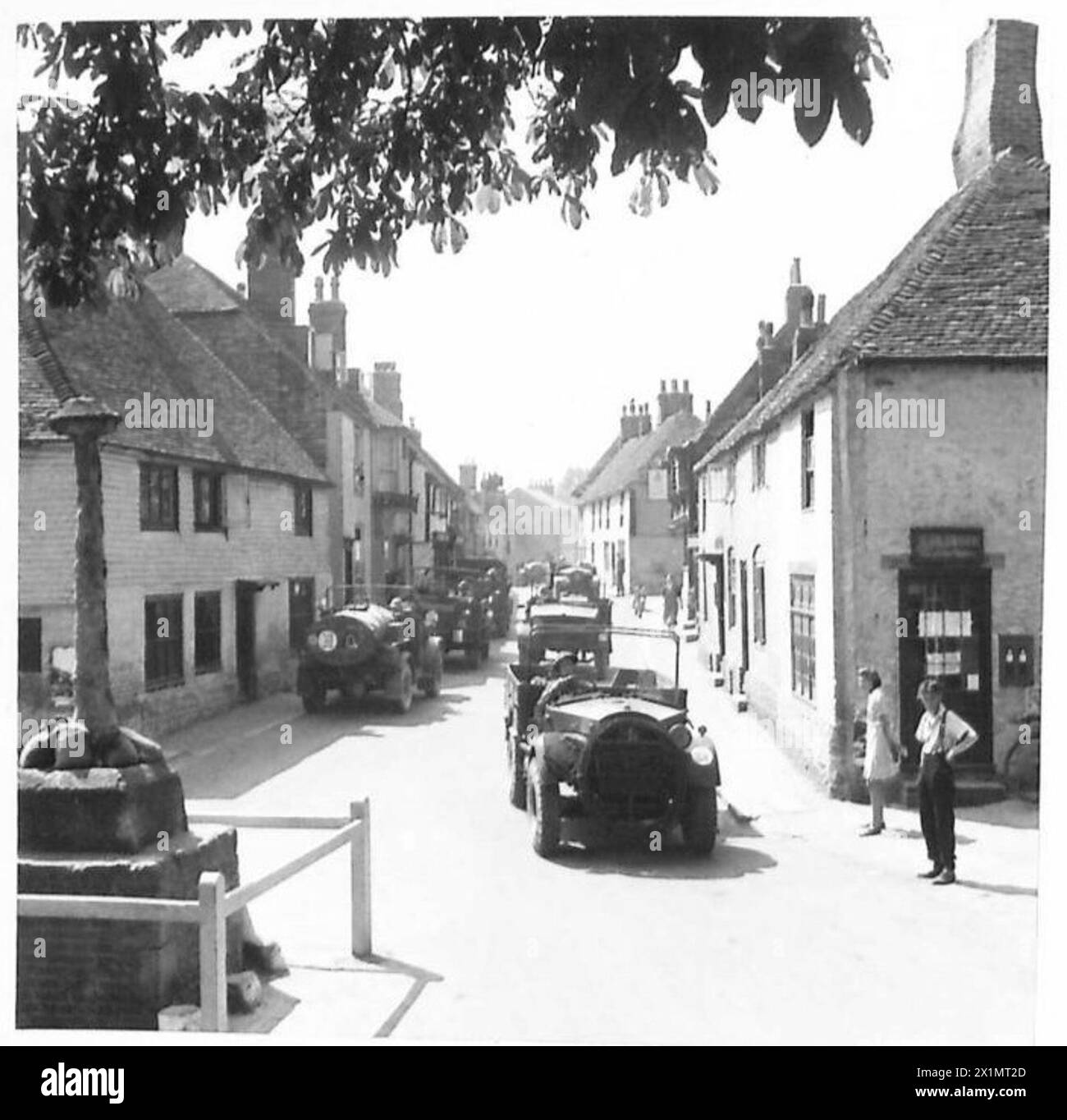Bren-Träger fahren durch ein historisches Dorf in Richtung Bahnhof und stellen moderne Militärfahrzeuge mit jahrhundertealter Architektur, der britischen Armee, gegenüber. Stockfoto