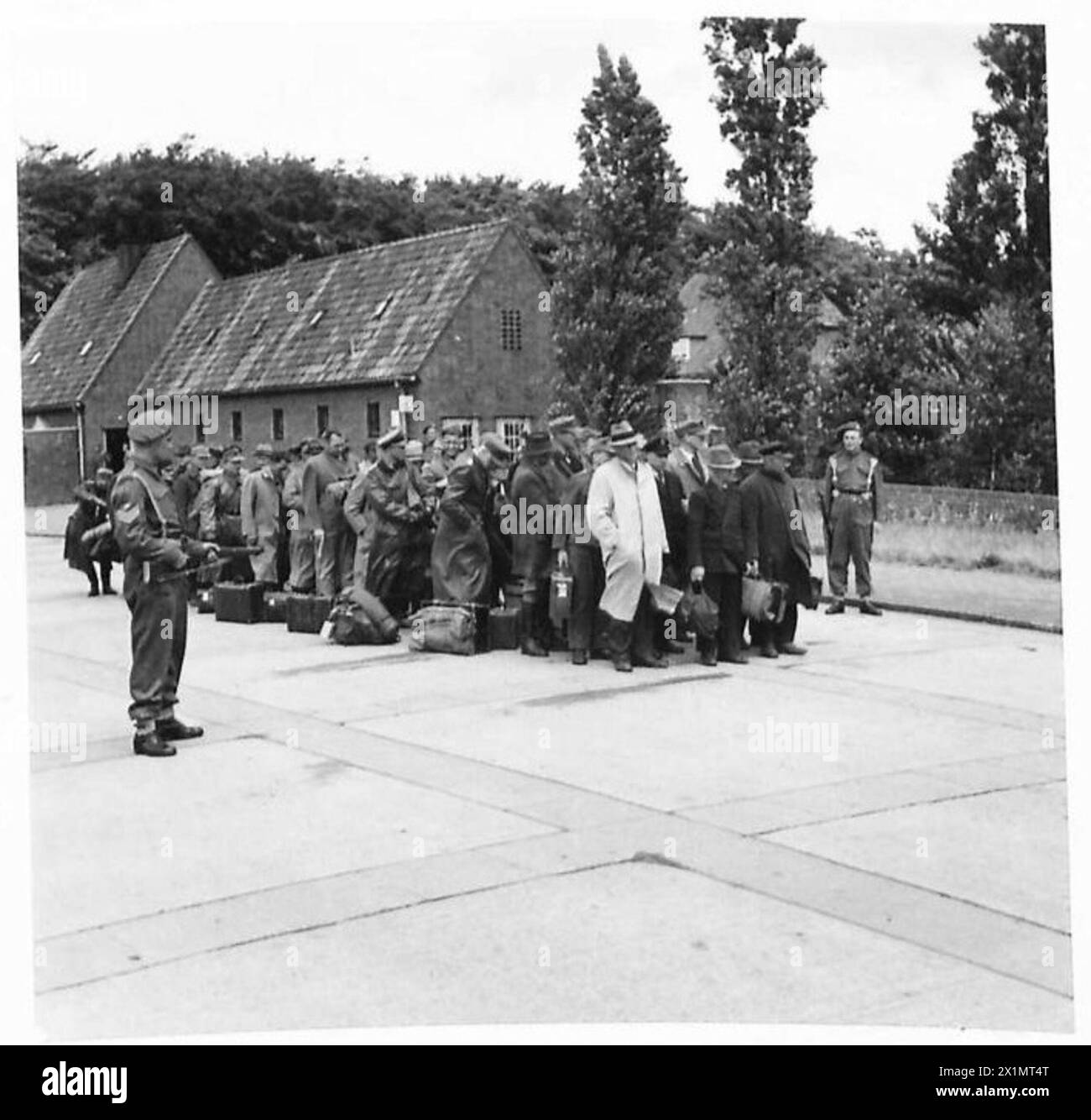 Neu angekommene deutsche politische Gefangene stellen sich beim Betreten des Lagers vor dem Verwaltungsgebäude unter der Aufsicht der britischen Armee, der 21. Armeegruppe. Stockfoto