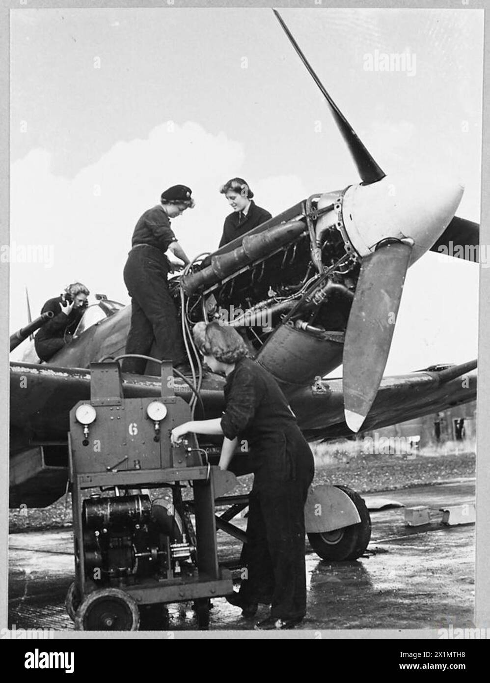 W.A.A.F. HELFEN BEI KAMPFFLUGOPERATIONEN - jedes Mal, wenn ein heimischer Sturm, Spitfire, Beaufighter oder Taifun in die Luft kommt, spielen W.A.F.-Mitarbeiter eine wichtige Rolle beim Erfolg des Piloten und des Flugzeugs. Das Bild (Ausgabe 1944) zeigt – auf einem Landefeld bedienen die Flugmechaniker die Druckpumpe und füllen die Luftflasche, die als Notentriegelung für das Spitfire-Laufwerk dient. Zur gleichen Zeit testet ein drahtloser Mechaniker die R/T, über die der Pilot mit der Basis der Royal Air Force kommuniziert Stockfoto