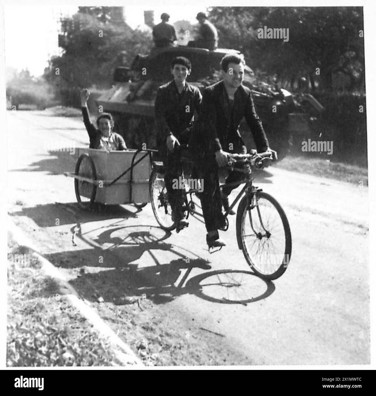 Ein Tandemfahrrad bringt eine Familie zurück nach Flers, was die Rückkehr von Zivilisten nach dem Kampf in Gebiete veranschaulicht, die vom Vormarsch der britischen Armee durch Frankreich während des Zweiten Weltkriegs unter der 21. Armeegruppe betroffen waren. Stockfoto