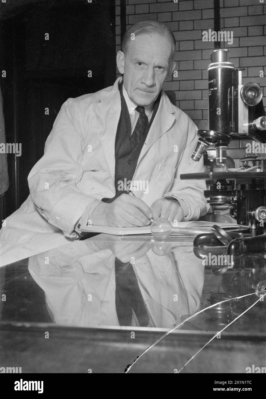 PENICILLIN VERGANGENHEIT, GEGENWART UND ZUKUNFT: ENTWICKLUNG UND PRODUKTION VON PENICILLIN, ENGLAND, 1944 - Professor Sir Robert Robinson sitzt neben seinem Mikroskop in einem Labor der Universität Oxford. Sir Robert, zusammen mit Dr. Chain und Dr. Abraham von der Pathologischen Schule, versucht synthetisches Penicillin herzustellen. Seit 1930 ist er Waynflete Professor für Chemie in Oxford und seit 1940 Mitglied des Privy Council Committee for Scientific and Industrial Research. Stockfoto